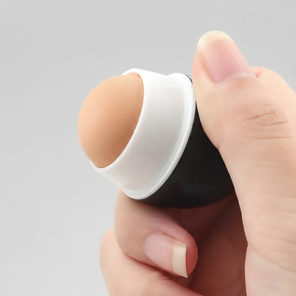 Hand holding a makeup sponge applicator with a white handle and brown foam pad on a white background